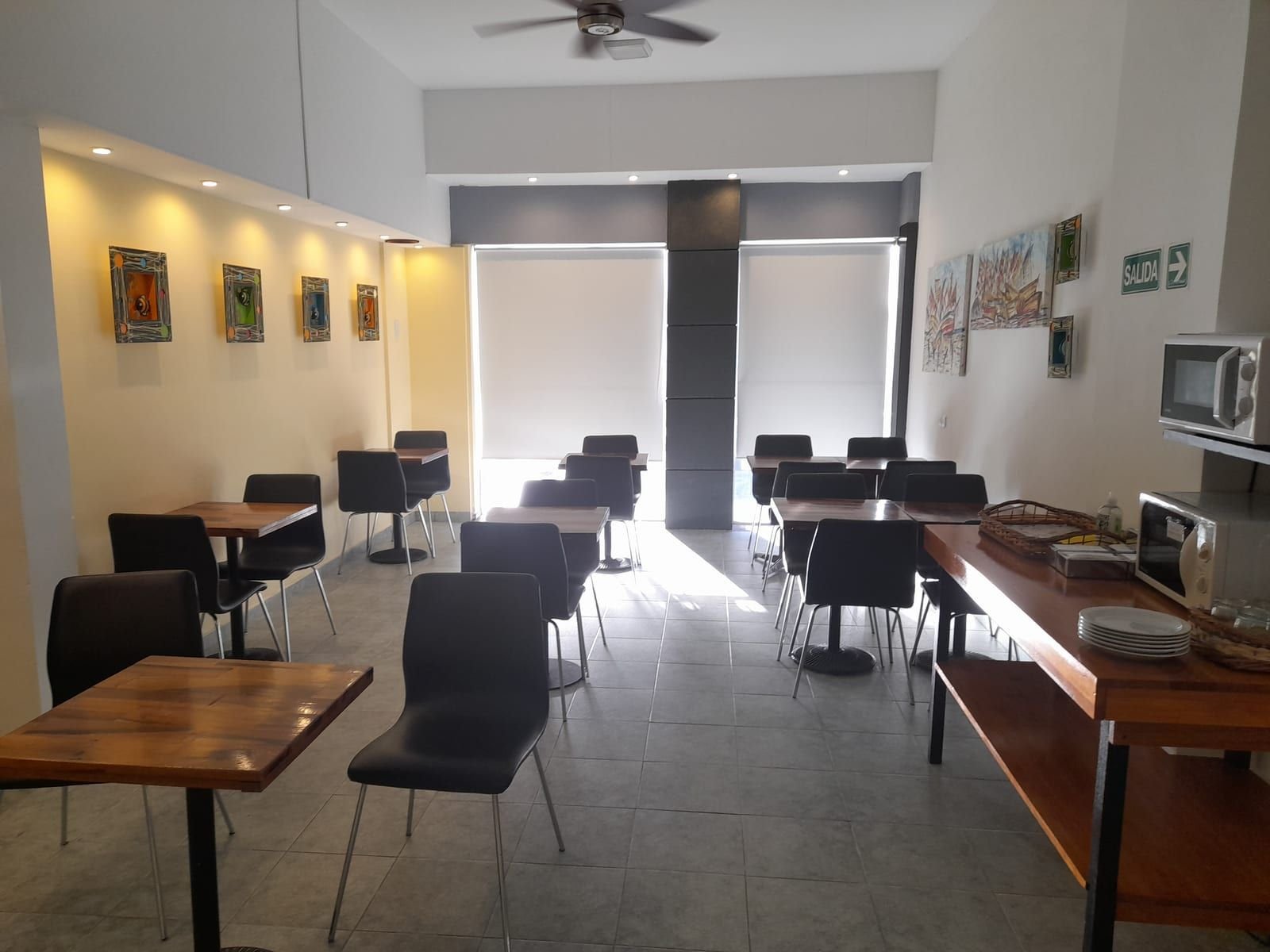 Salón comedor del hotel con mesas de madera, sillas negras y un mueble con vajilla y microondas
