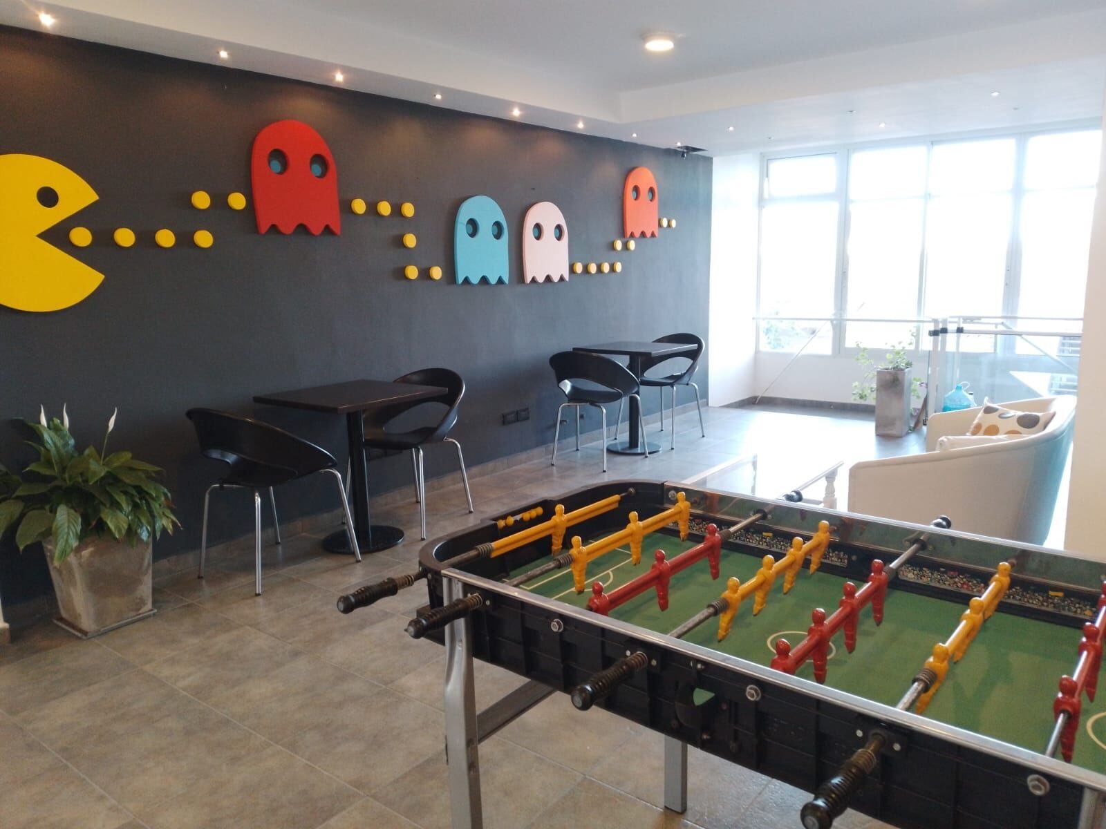 Sala de juegos con metegol, mesas y la pared decorada con figuras de un videojuego clásico